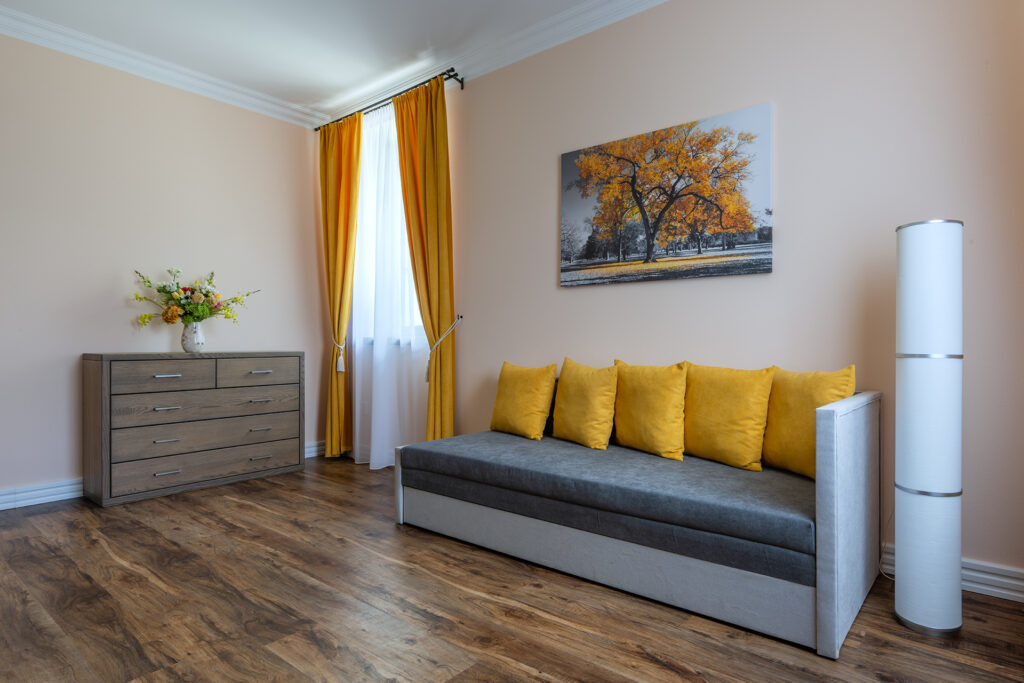 Pod Krásnou horou - pokoj Jantar - záběr okna a rozkládacího gauče - žluté prvky na polštářích a závěsech